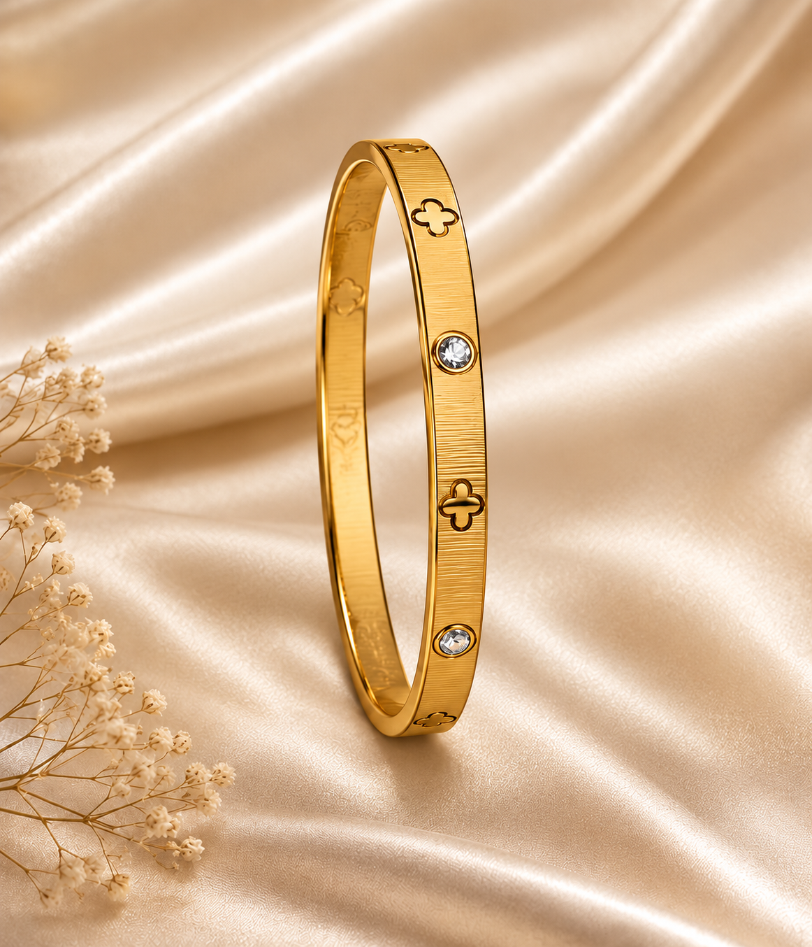 One gold four-leaf motif bangle with zirconia accents on champagne satin