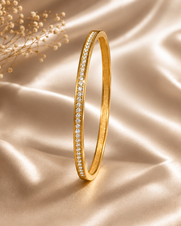 One slim gold bangle with a single row of clear zirconia stones on champagne satin