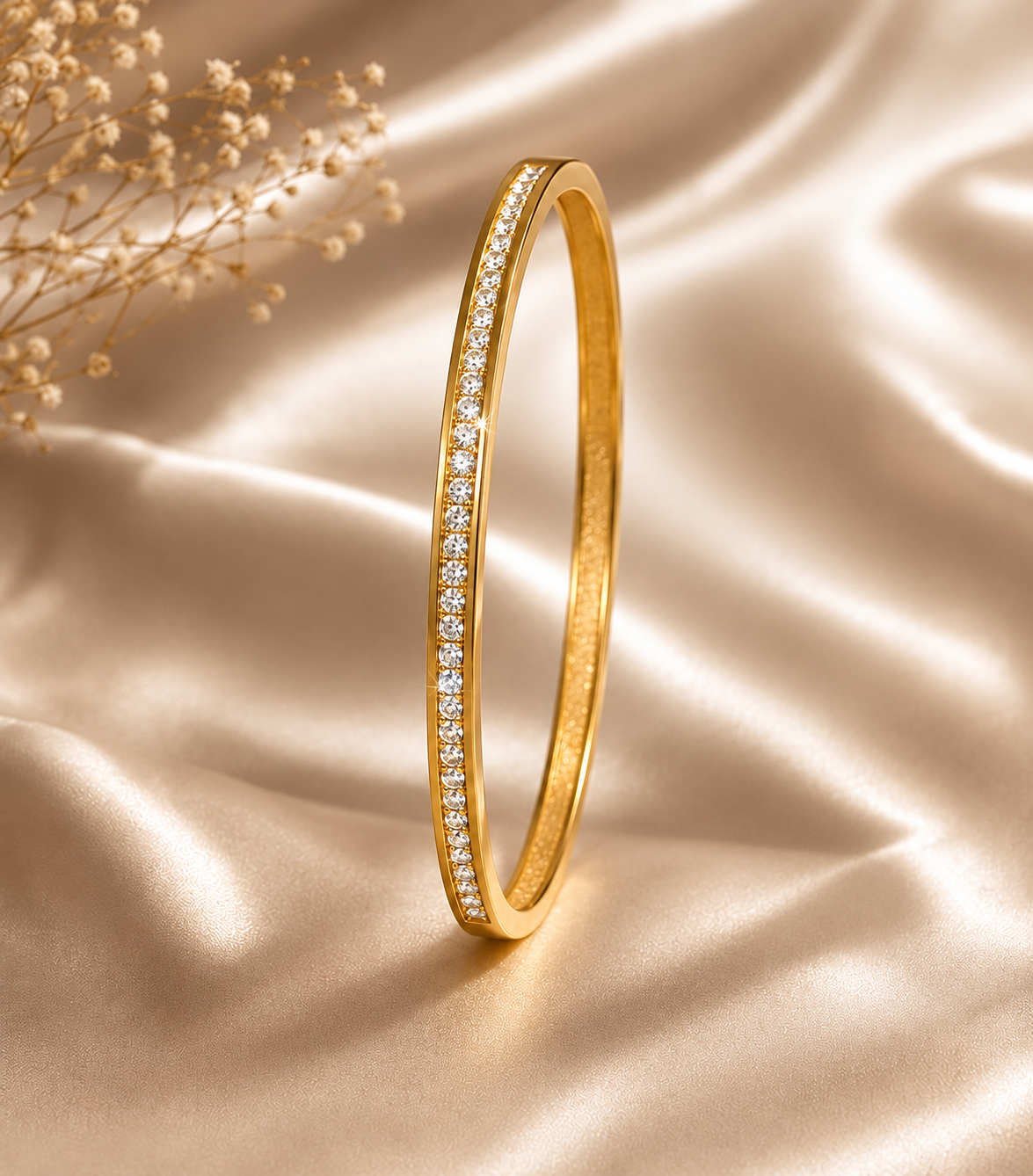 One slim gold bangle with a single row of clear zirconia stones on champagne satin